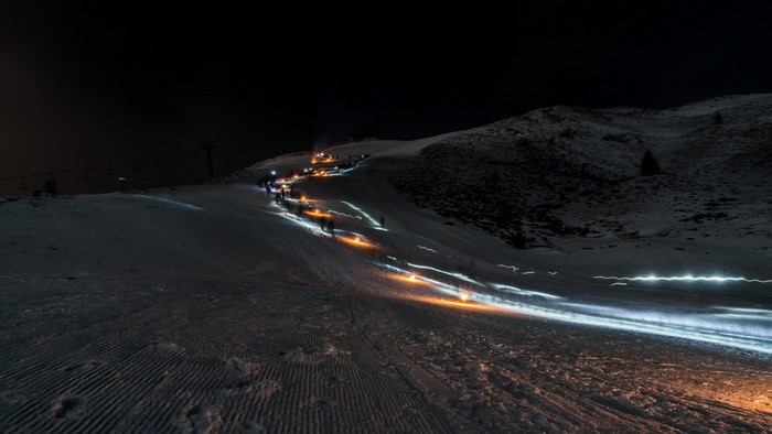 People skiing down a snowy mountain at night with torches