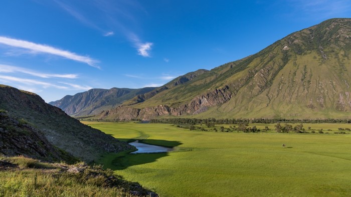 Green valley with river and mountains under blue sky