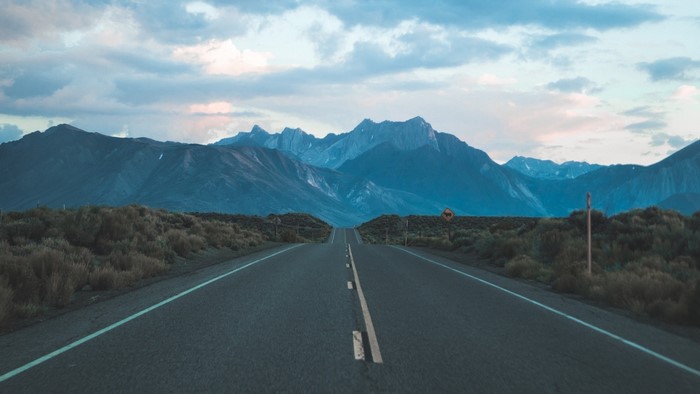 Road leading to mountains under cloudy sky