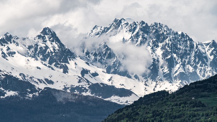 Snow-capped mountains with clouds and green foothills