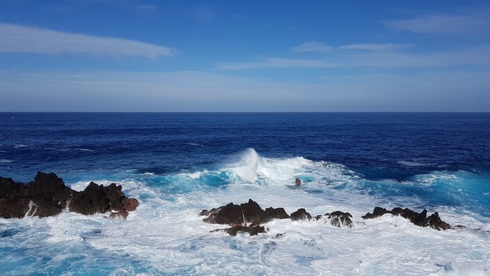 Ocean waves crashing on rocks under a blue sky