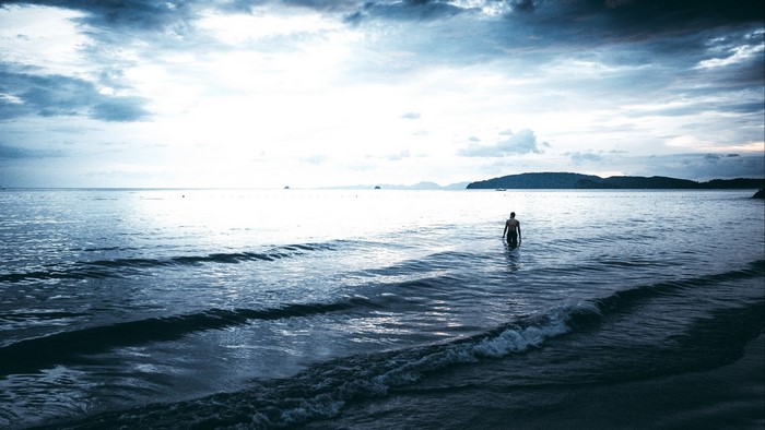 Man wading into the ocean under cloudy sky