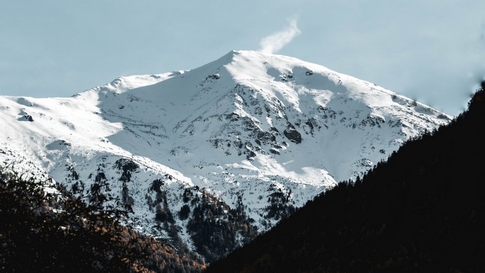 Snowy mountain peak with a plume of smoke