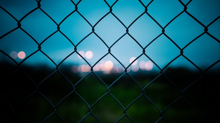Chain-link fence against a twilight sky with bokeh lights