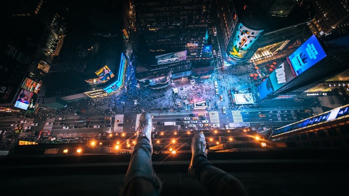 Person sitting on edge of building overlooking Times Square at night