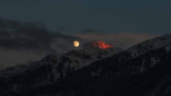Full moon over snow-capped mountains at dusk