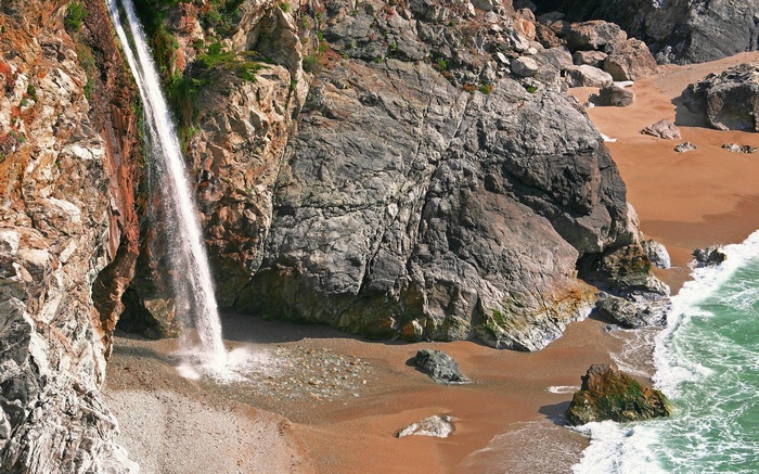 Waterfall cascading onto a sandy beach with ocean waves