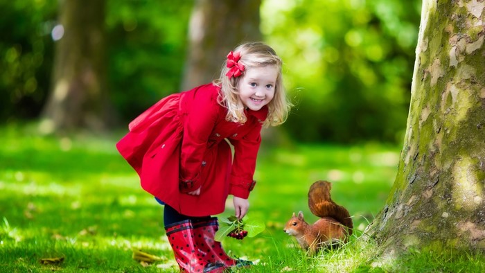 Girl in red coat with squirrel in park