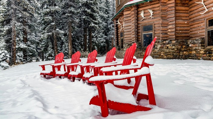 Red Adirondack chairs in the snow outside a log cabin