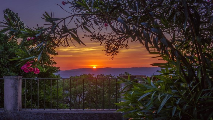 Sunset over mountains viewed from a balcony with plants