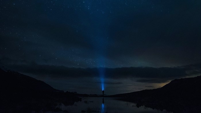 Person with flashlight under starry sky