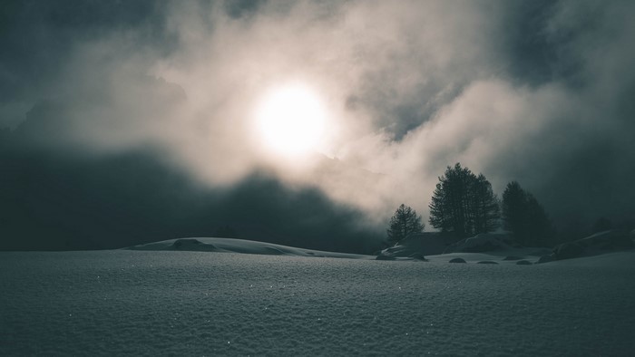 Snowy landscape with sun obscured by clouds