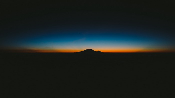 Silhouette of a mountain against a sunset gradient