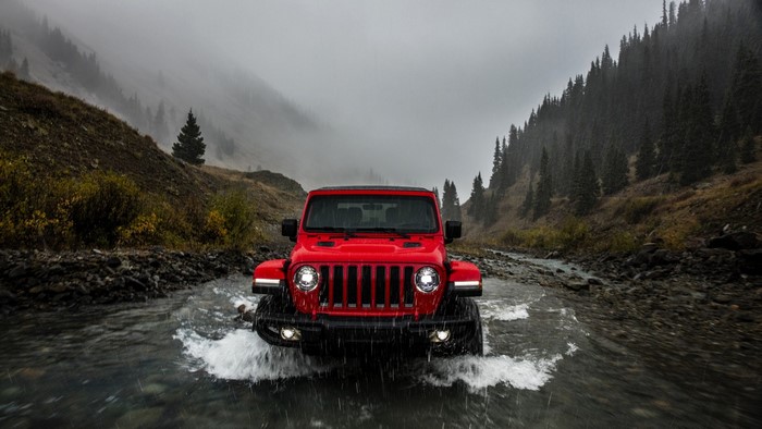 Red Jeep Wrangler driving through a stream