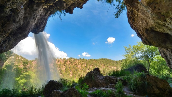 View from a cave overlooking a waterfall and forested hills