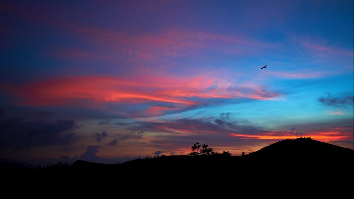 Airplane flying over silhouetted hills at sunset