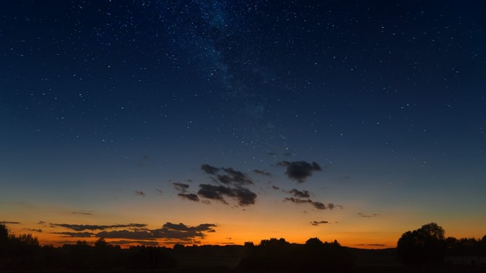 Starry night sky over a silhouetted landscape