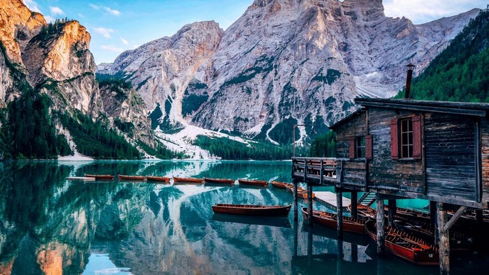 Wooden cabin on a lake with boats and mountains