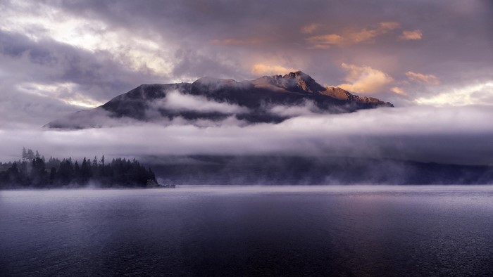 Mountain peak emerging from clouds over a misty lake