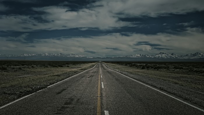Road leading to snow-capped mountains under cloudy sky