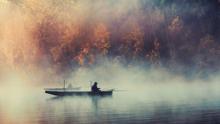 Two fishermen in boats on a misty lake at sunrise