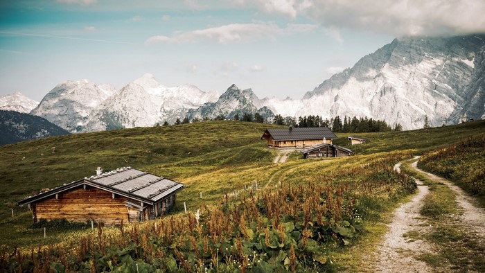 Wooden cabins on a grassy mountain slope with a dirt road