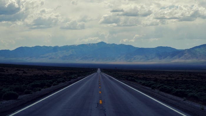 Long empty road leading to mountains under cloudy sky
