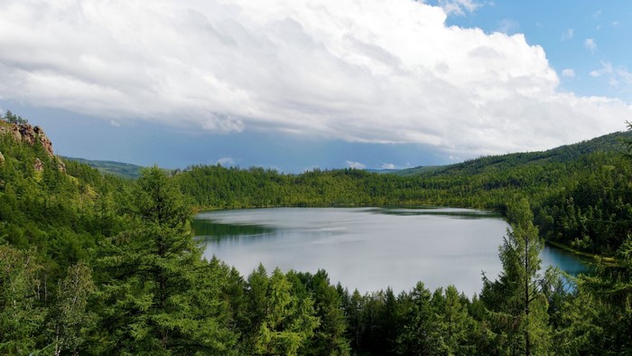 Lake surrounded by green forest and mountains under cloudy sky