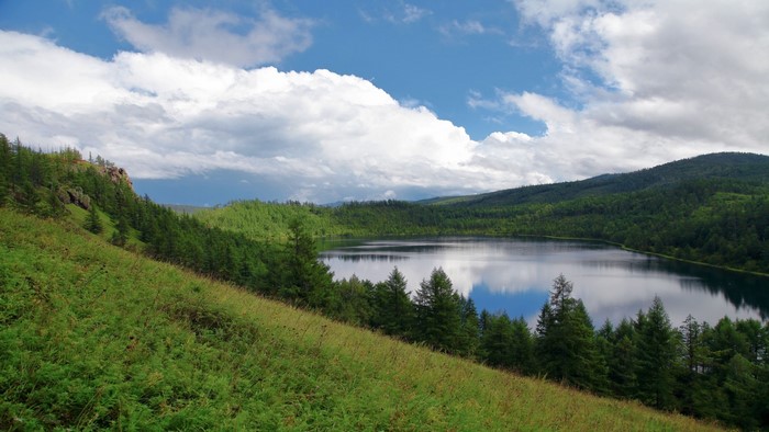 Lake surrounded by green forest and hills under a cloudy sky