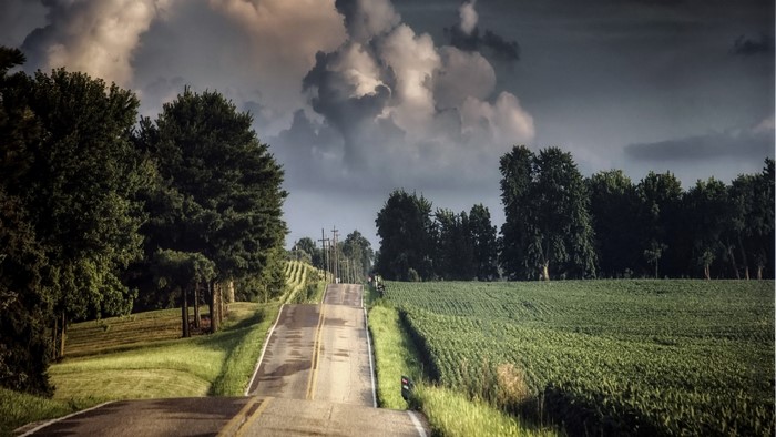 Road through farmland under stormy clouds