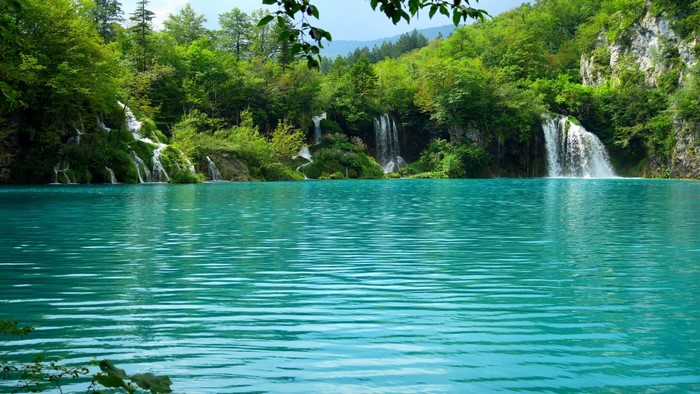 Turquoise lake with waterfalls and green forest