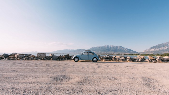 Blue Volkswagen Beetle by a lake with mountains