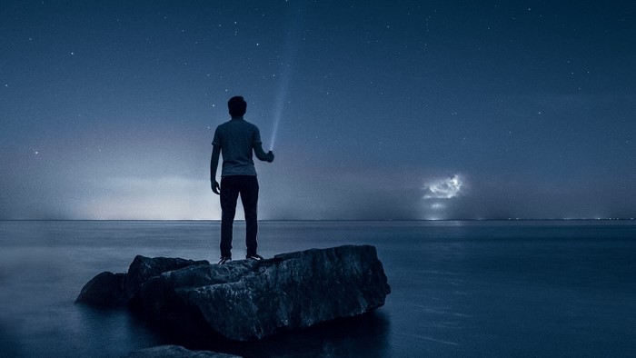 Man with flashlight on rocks at night