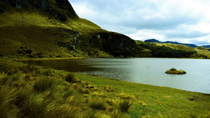 Lake and grassy hills under cloudy sky