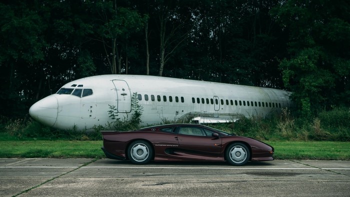 Jaguar XJ220 parked next to a derelict airplane