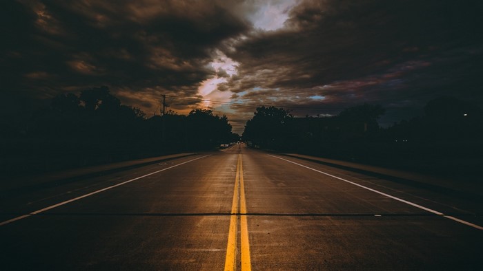Empty road with double yellow lines under stormy clouds