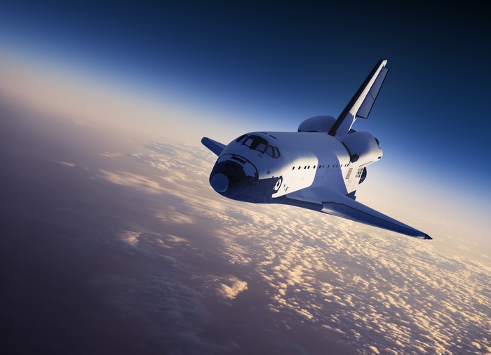 Space shuttle flying above clouds at sunset