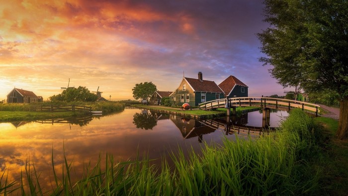 Dutch windmills and houses by a canal at sunset