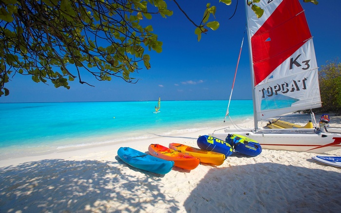 Beach with kayaks, sailboat, and windsurfer