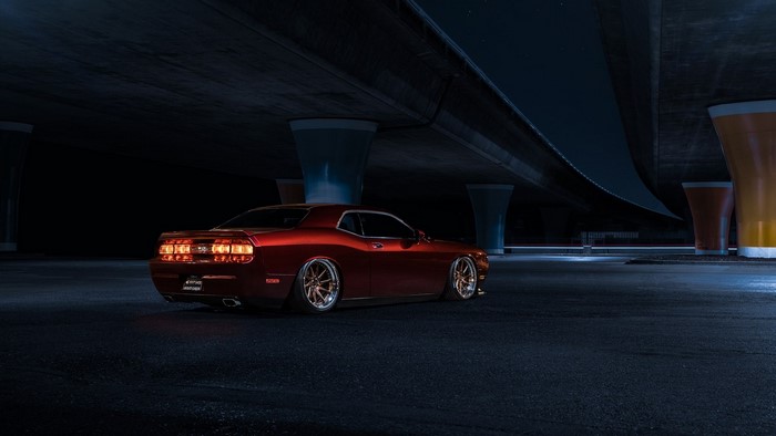 Red Dodge Challenger parked under a bridge at night