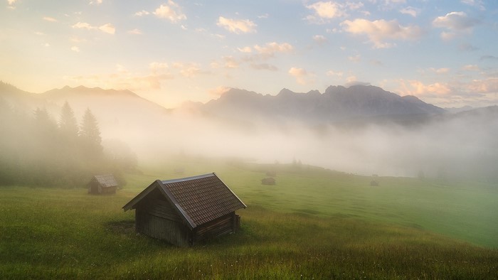 Wooden huts in foggy Bavarian Alps at sunrise