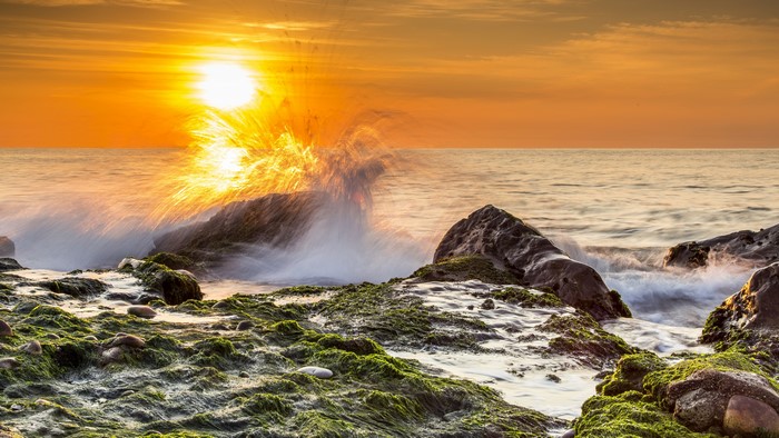 Wave crashing on rocks at sunset