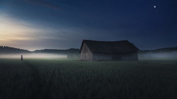 Person and barn in foggy field under starry sky