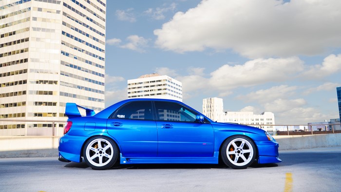 Blue Subaru Impreza with white rims in front of buildings