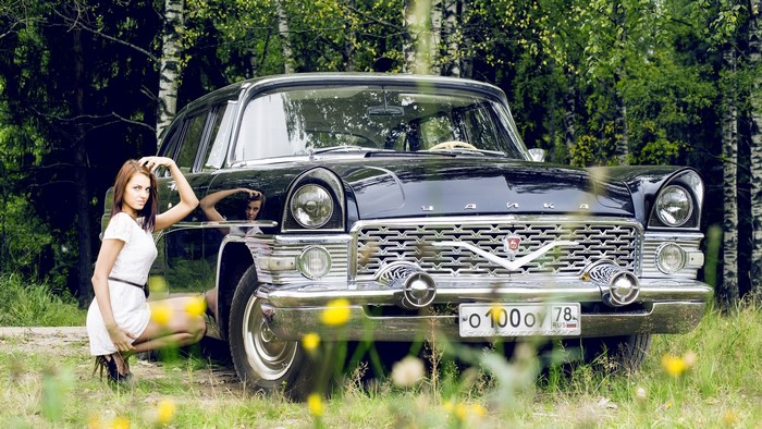 Woman posing by a vintage black car in a forest