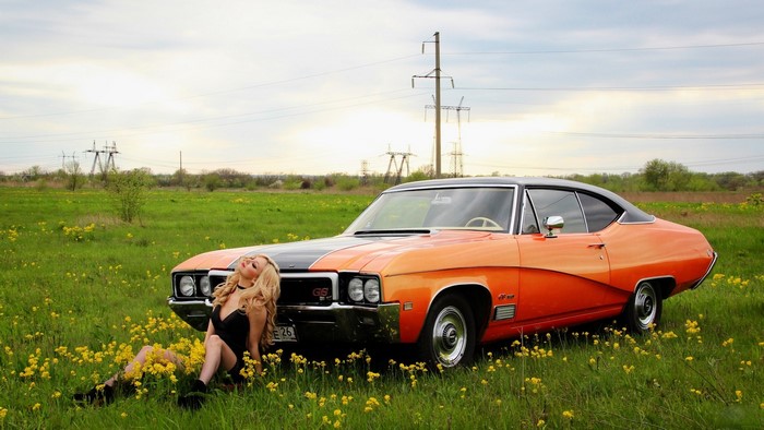 Woman in black dress with retro orange car in field