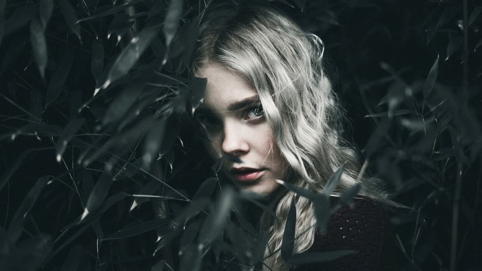 Blonde woman peeking through dark foliage