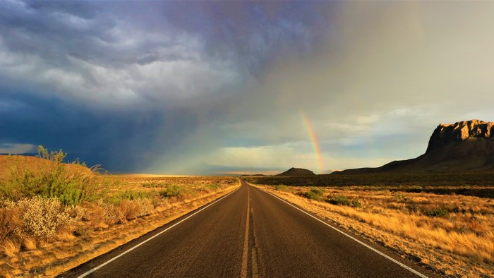 Road through desert landscape with rainbow