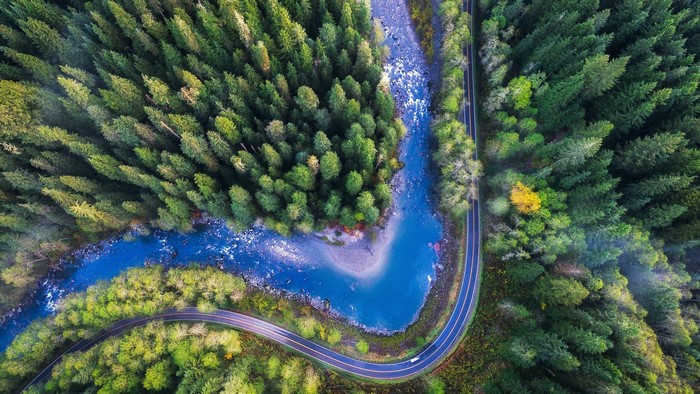 Aerial view of a winding road next to a river and forest