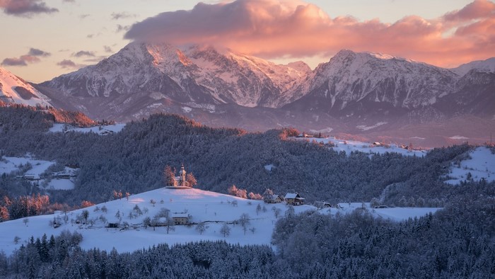 Snowy mountains with a church on a hill at sunset